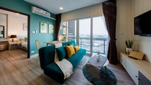 Een moderne woonkamer met een blauwgroene bank, een eethoek, een televisie en een balkon met uitzicht op de stad.