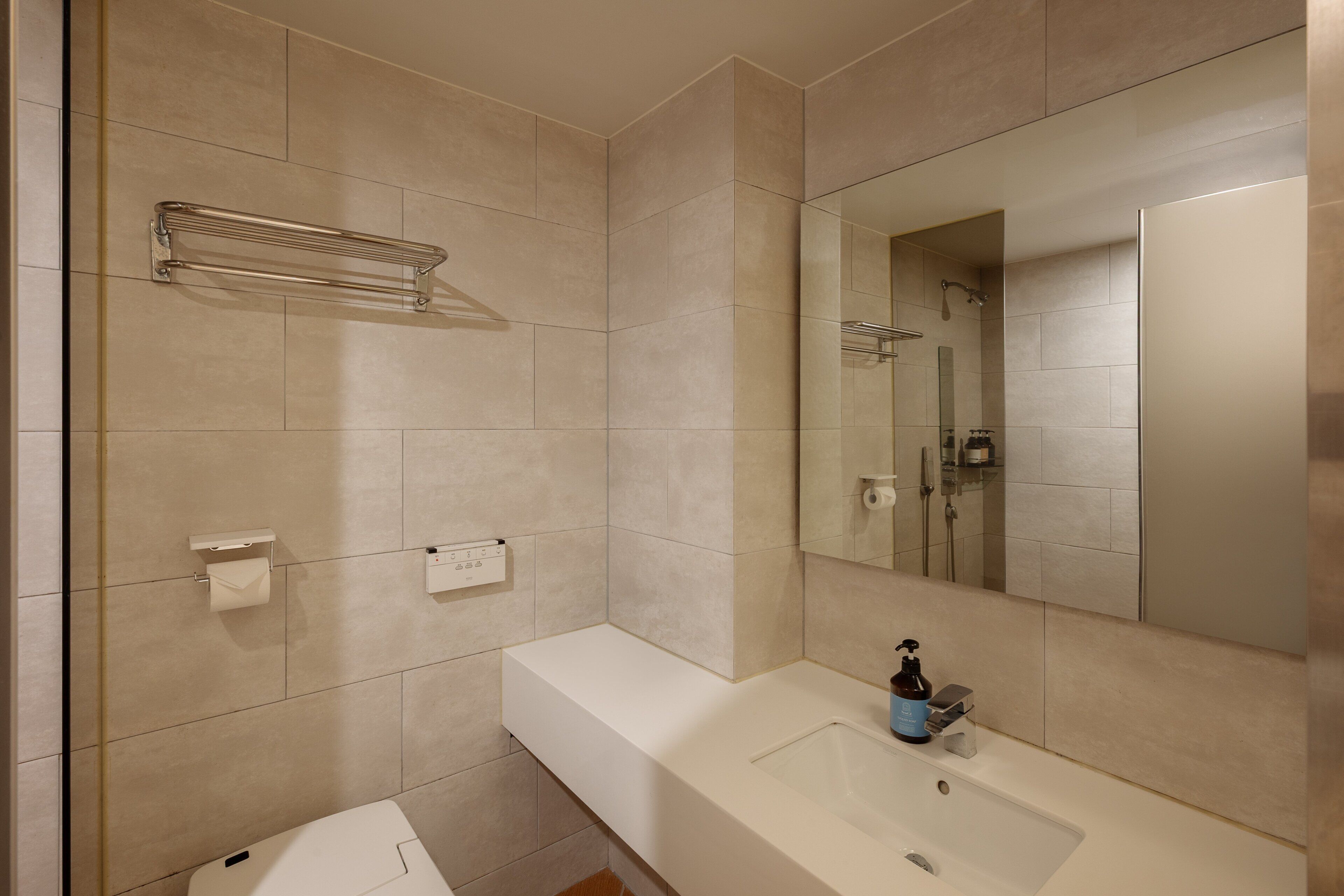 A modern bathroom with a large mirror, a white sink, and a toilet.