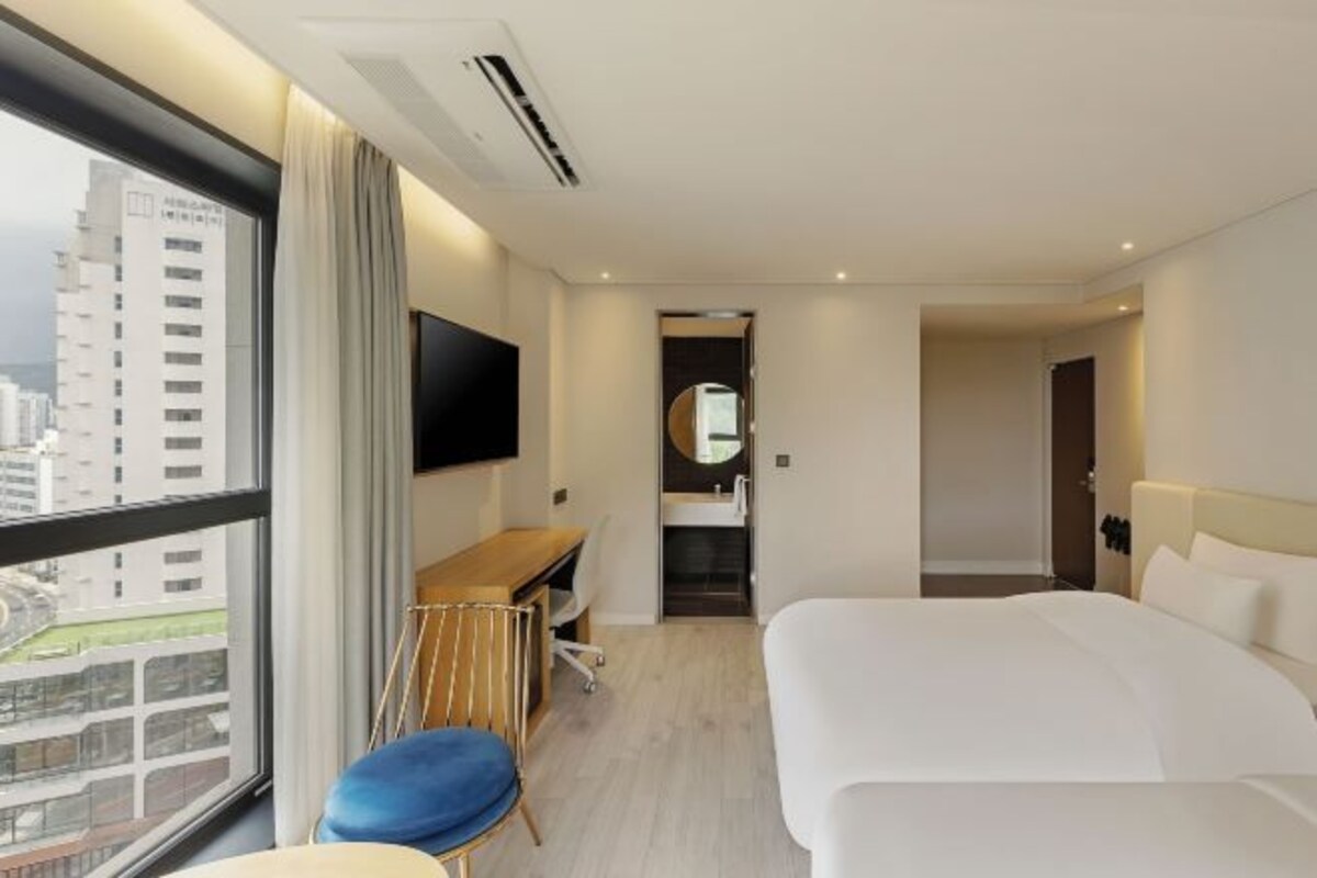 Habitación de hotel con cama, escritorio, silla, televisor y vista a la ciudad.