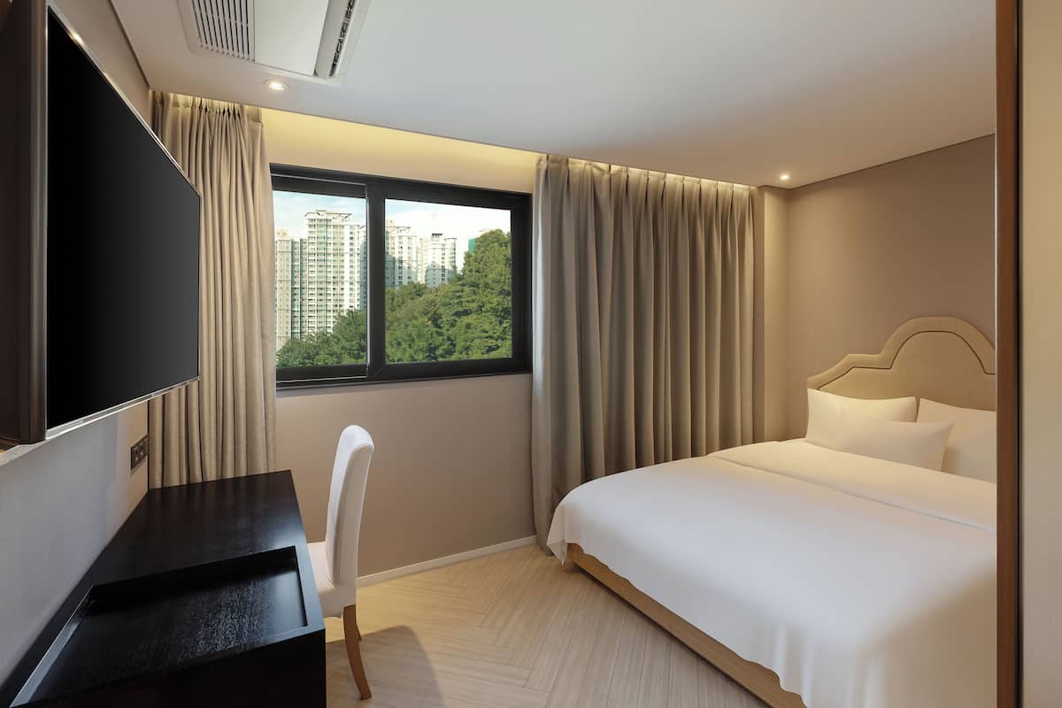 A hotel room with a bed, a desk, a chair, a TV, and a window with curtains.