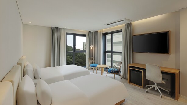 A modern hotel room with two beds, a desk, a chair, a TV, and large windows with curtains.