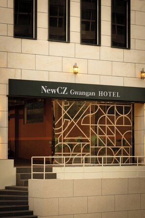 Az új NewCZ Gwangan Hotel külső megjelenése modern homlokzattal, feltűnő bejárattal és díszes üvegpanellel rendelkezik.