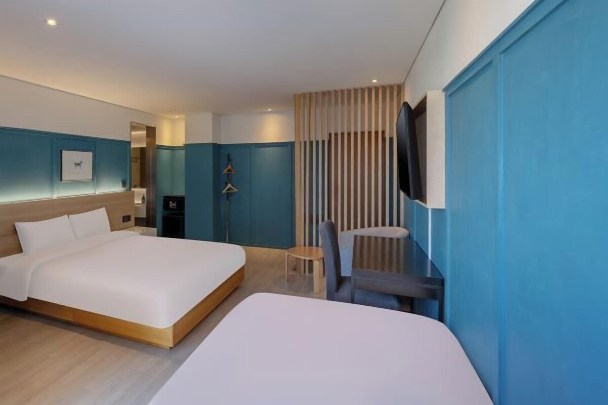 Habitación de hotel con dos camas, un televisor montado en la pared y una pequeña mesa con una silla.