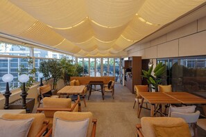 Un intérieur moderne avec un plafond haut, de grandes fenêtres et différents types de mobilier, notamment des tables et des chaises.