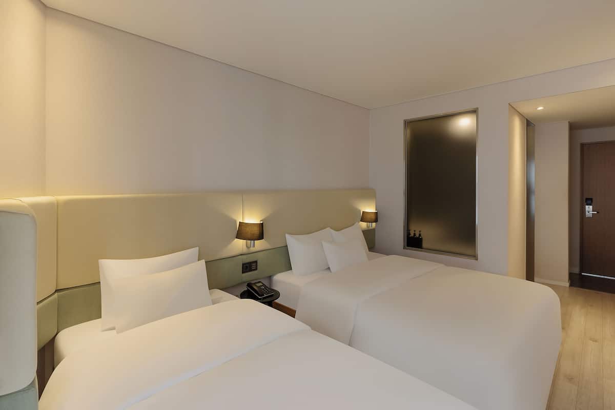 A hotel room with two beds, a bedside table with a phone, and wall-mounted lamps.