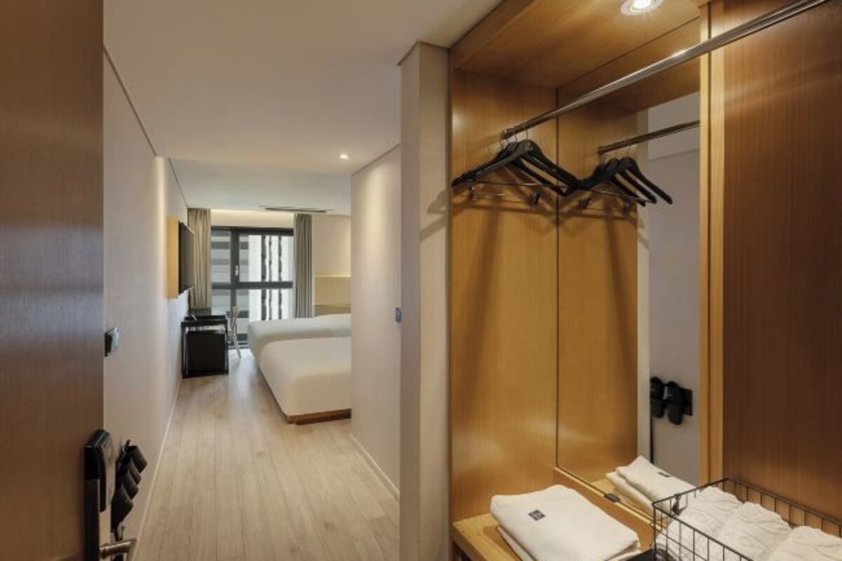 Una habitación de hotel con un armario de madera, una cama, una mesita de noche y un perchero.