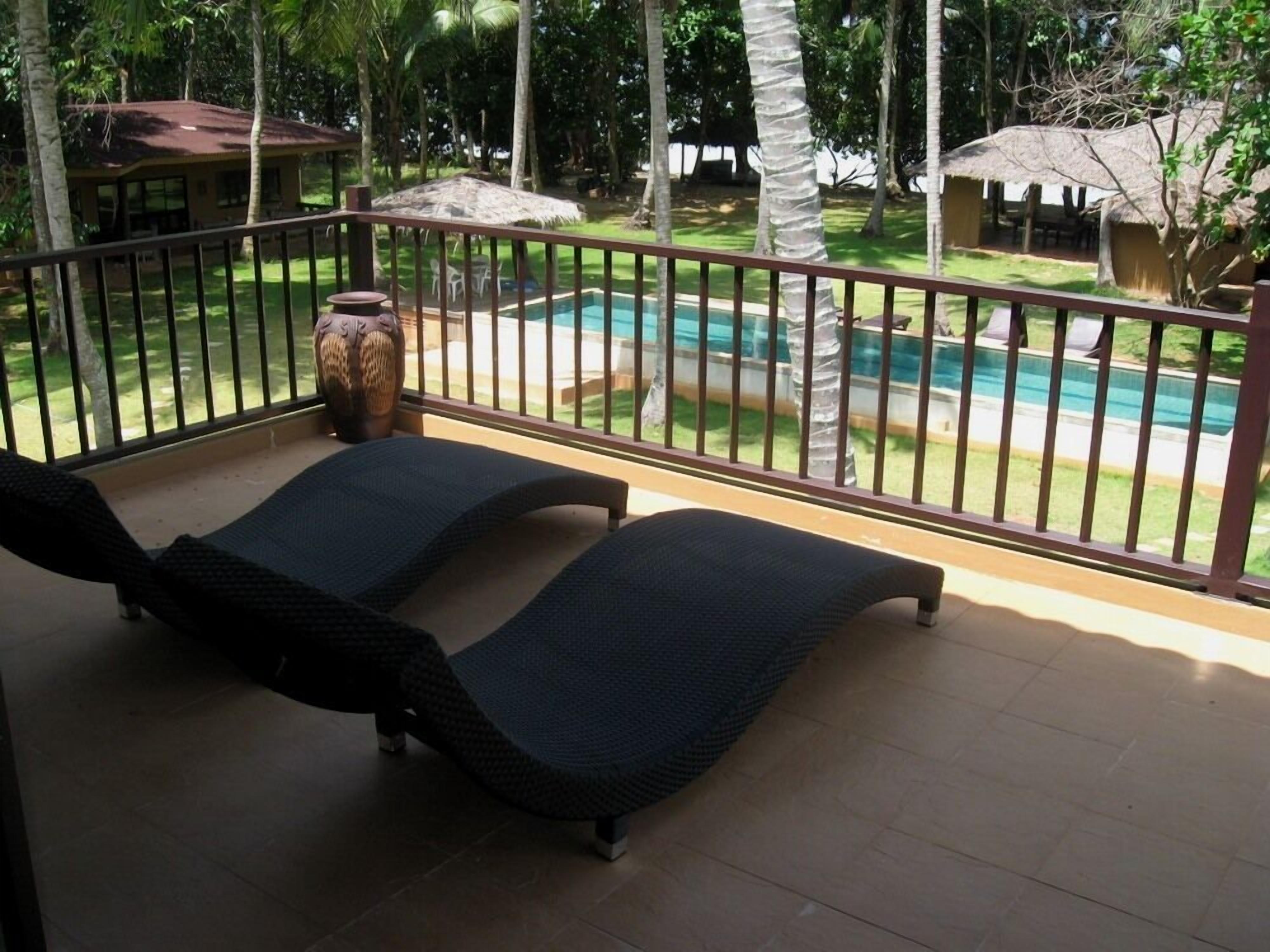 Un balcon avec deux fauteuils, un grand vase et une piscine en arrière-plan.