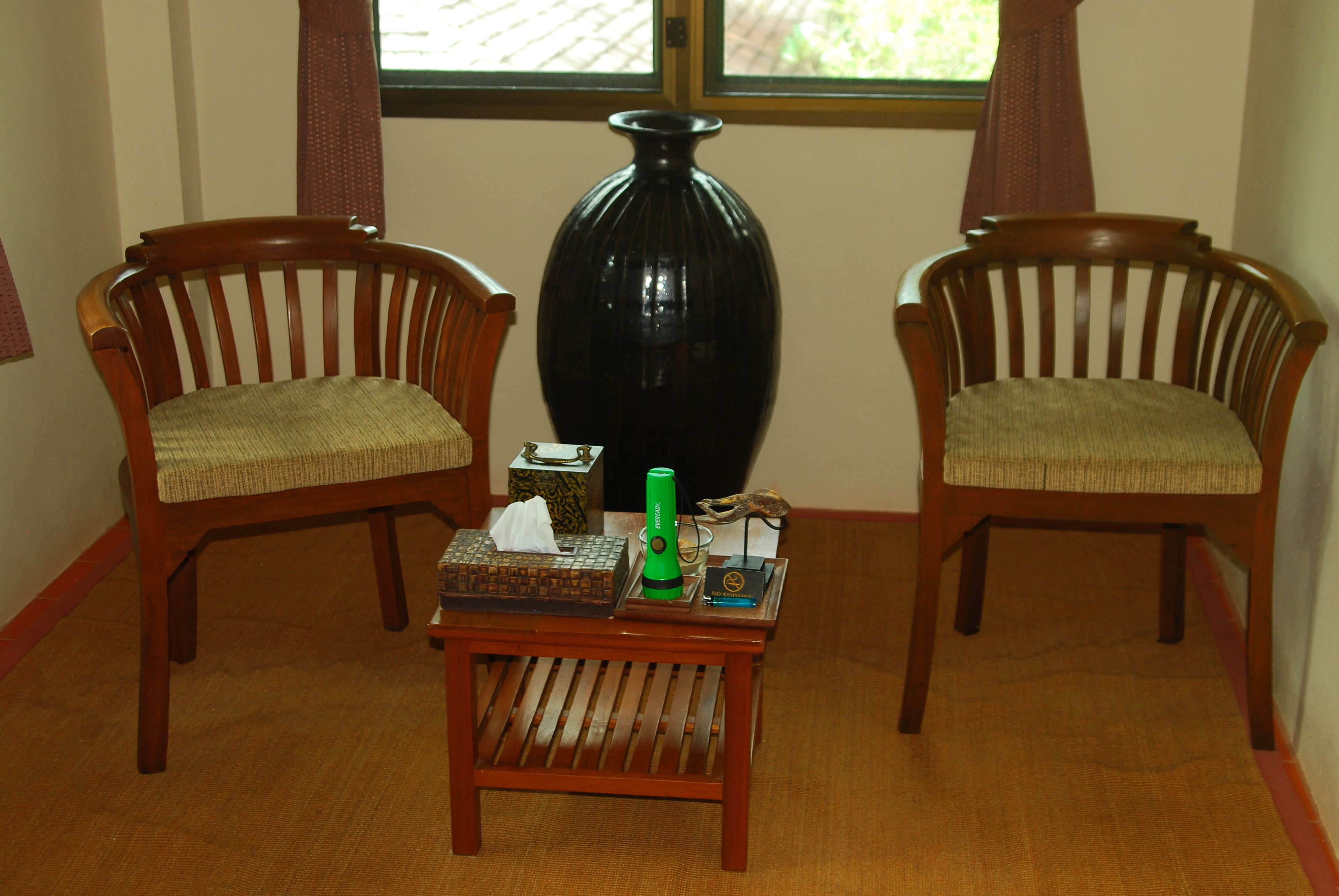Two wooden chairs with woven seats, a small wooden table with a tissue box, a green bottle, and a decorative item between them.