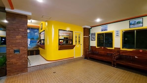 Un espace d’accueil avec un mur jaune, un comptoir de réception, un banc et un revêtement de sol carrelé.