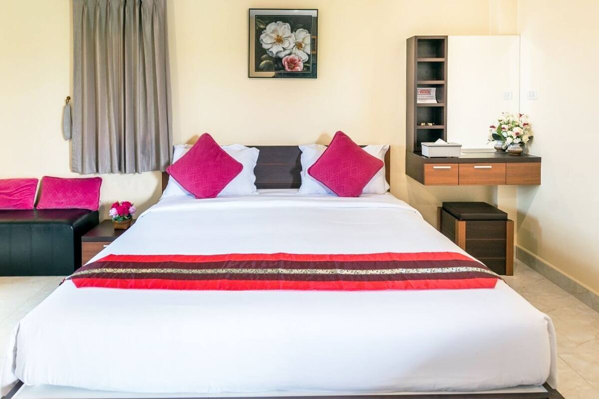 A hotel room with a large bed, a desk, a chair, a nightstand, and a mirror.