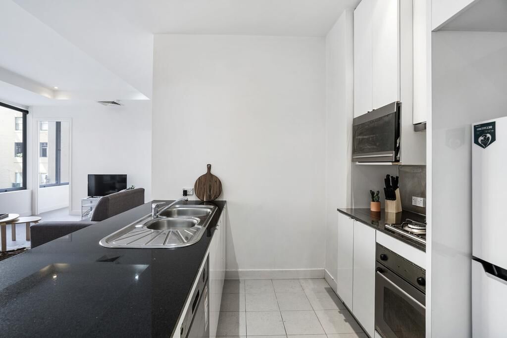 A modern kitchen with a black countertop, stainless steel sink, and white cabinetry.