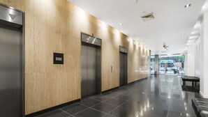 Uma área moderna de elevadores, com três elevadores, um banco e um chão limpo revestido de azulejos.