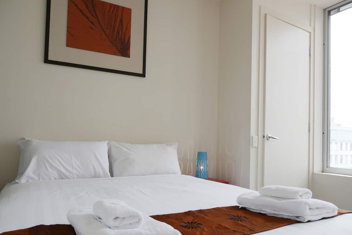 A neatly made bed with white linens, a brown throw blanket, and two folded towels.