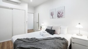 Quarto moderno com cama bem arrumada, mesa de cabeceira com abajur e ar-condicionado fixado na parede.