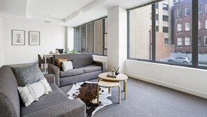 Sala de estar moderna com sofá cinzento, mesa redonda pequena e uma janela ampla com vista para a cidade.