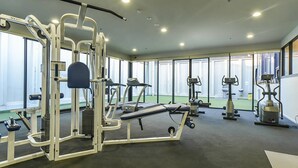 Ett gym med olika träningsmaskiner, stora fönster och ett golv med grön yta.