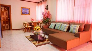 A living room with a brown sofa, a glass coffee table, a dining table with chairs, and a door with a decorative frame. - Phimaibury Apartment (Phimai)
