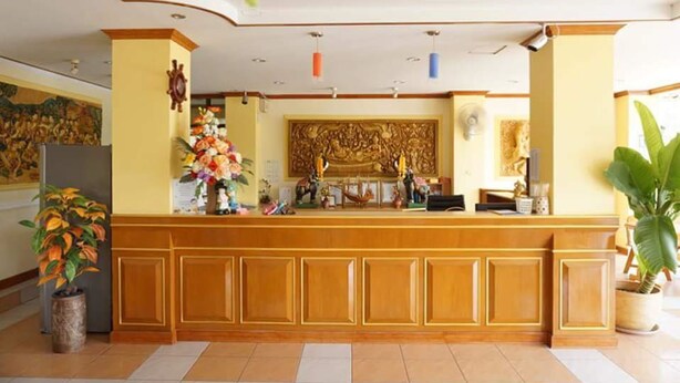 A reception area with a wooden reception desk, a large decorative wall piece, and potted plants. - Phimaibury Apartment (Phimai)