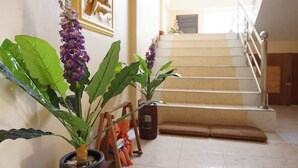 A staircase with a handrail, a small bench at the bottom, and potted plants on either side. - Phimaibury Apartment (Phimai)