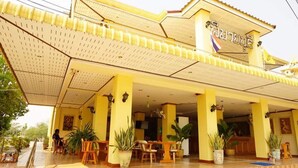 A hotel with a covered outdoor seating area, potted plants, and a sign with text. - Phimaibury Apartment (Phimai)