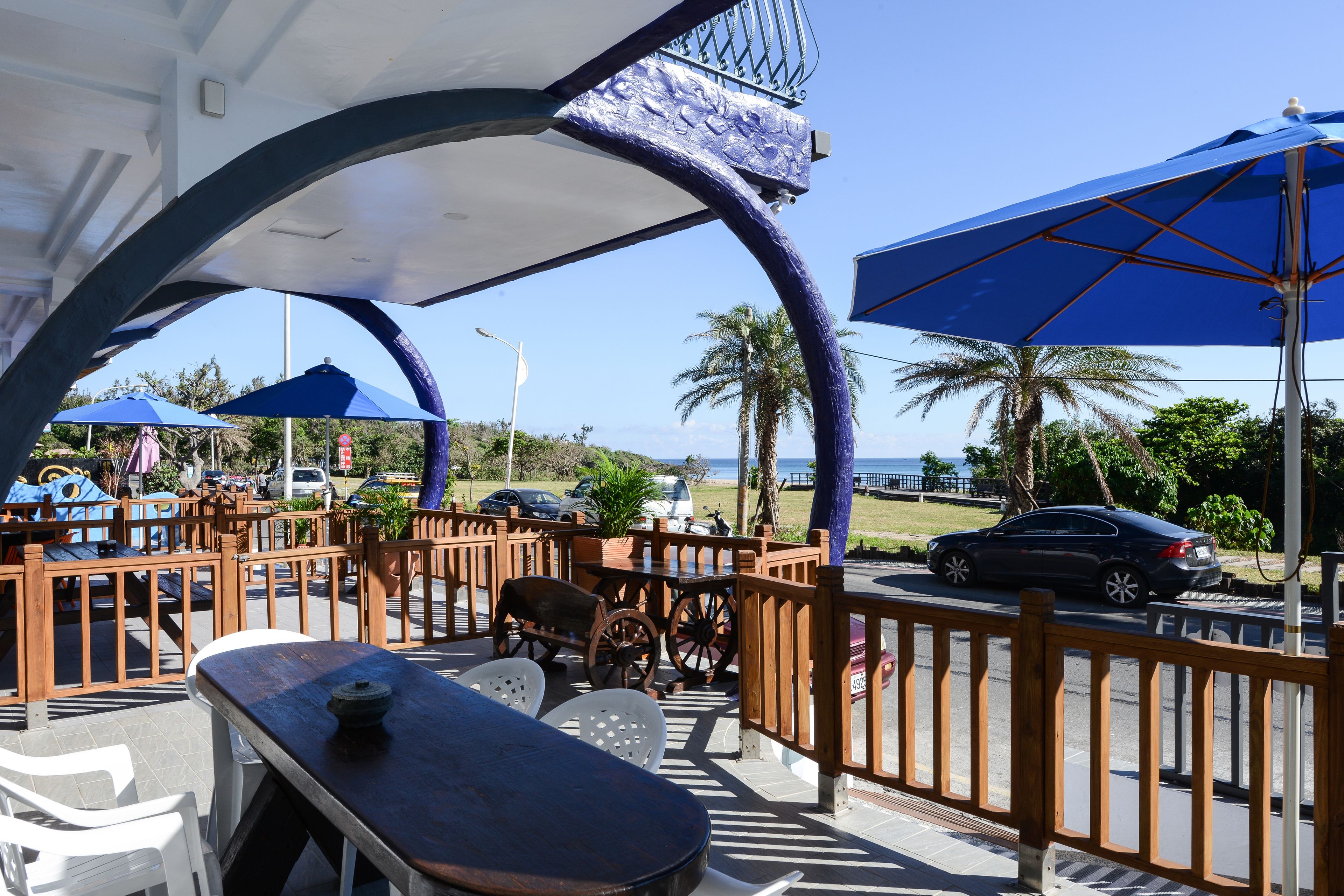 A covered outdoor seating area with tables and chairs, a wooden fence, and a view of the ocean.