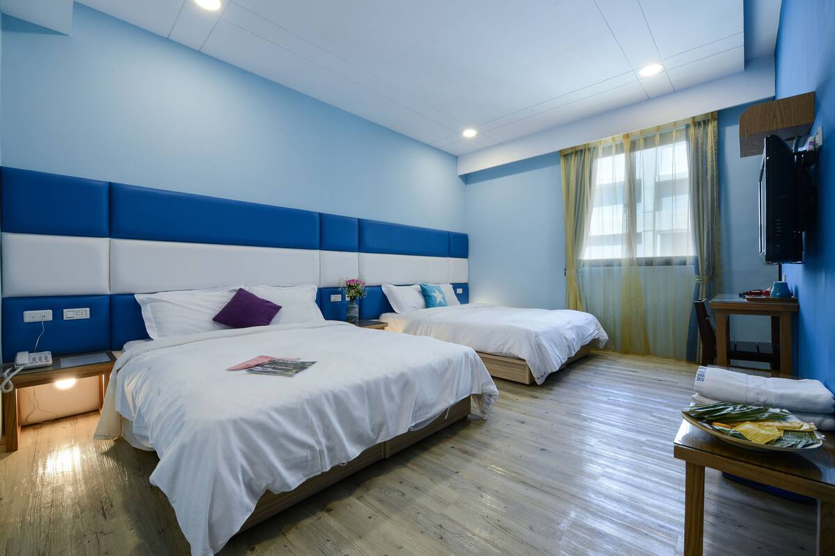 A hotel room with two beds, a wooden floor, a TV on the wall, and a table with towels.