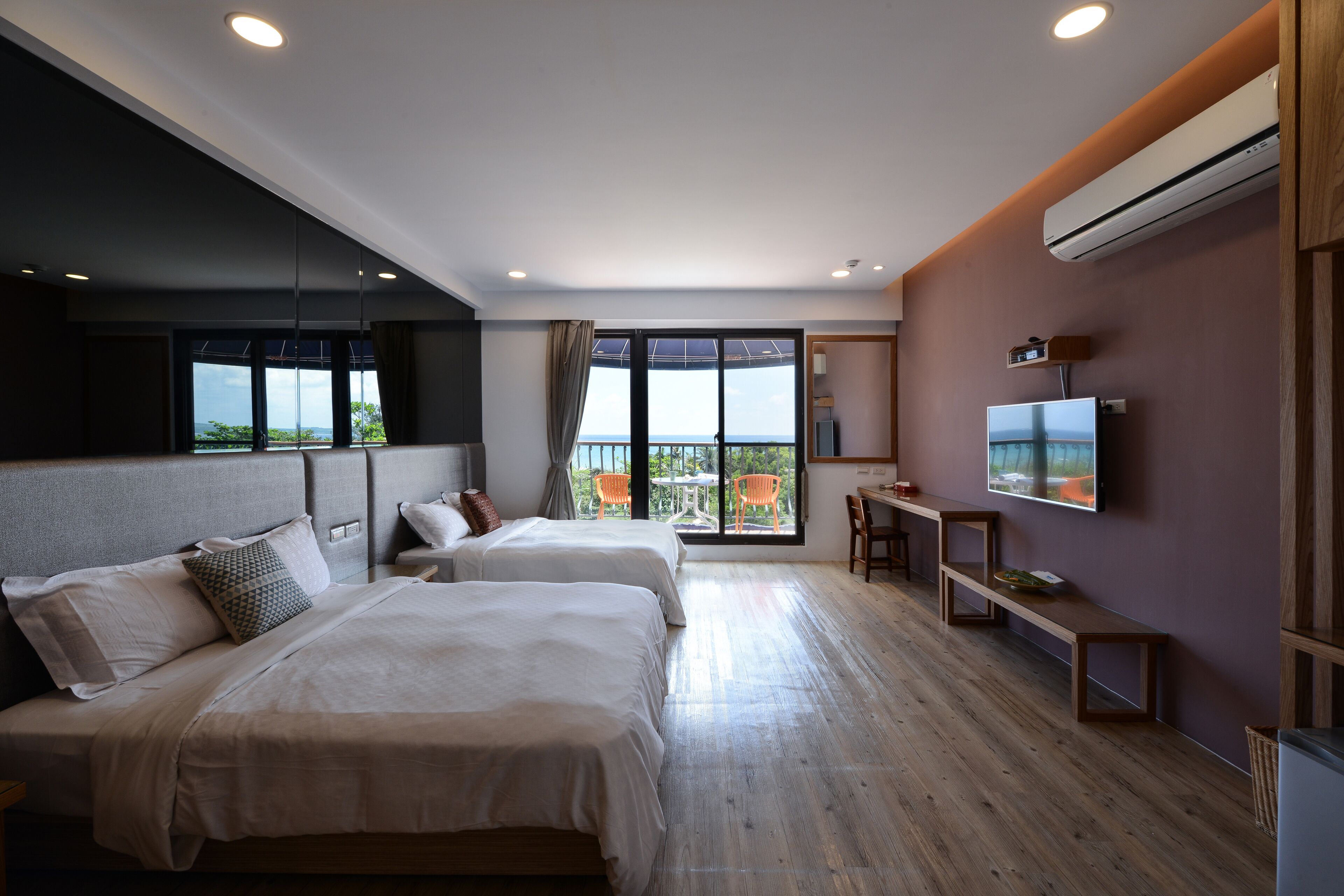 A modern hotel room with two beds, a TV, and a balcony with chairs.