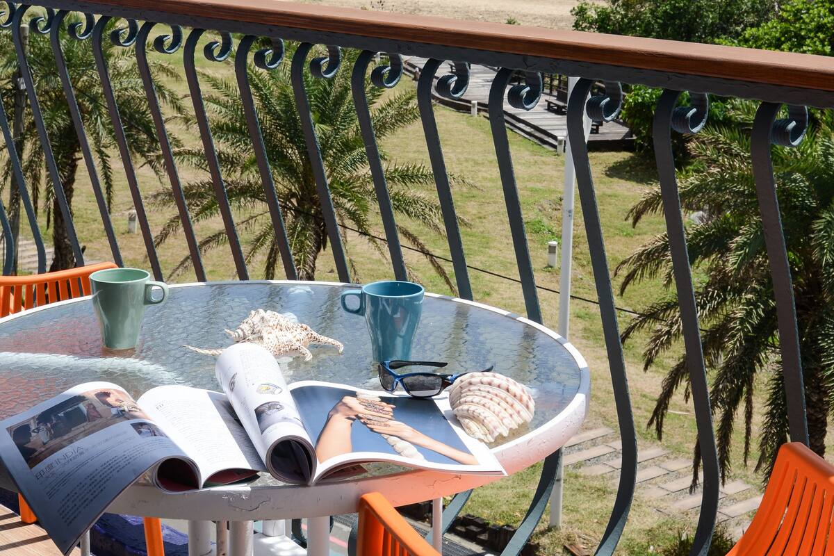 A balcony with a table and chairs overlooking a beach.