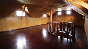 Een zolderkamer met houten wanden, een houten trap en twee dakramen.