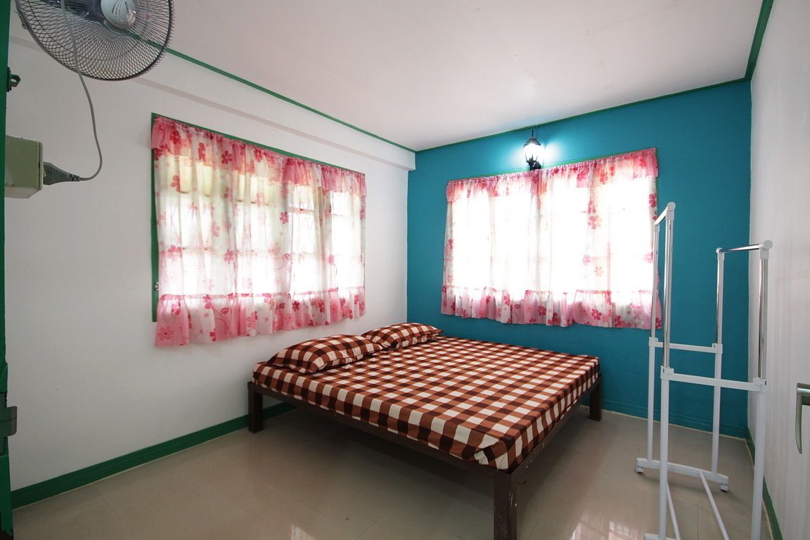 A bedroom with a bed, two windows with floral curtains, a standing fan, and a white ladder.