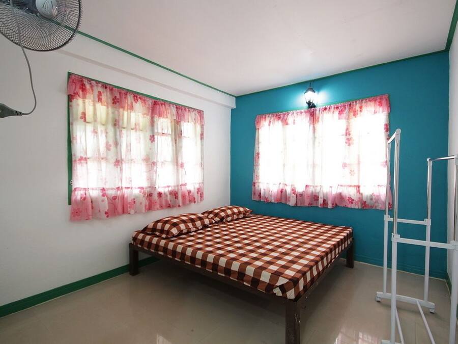 A bedroom with a bed, two windows with floral curtains, a standing fan, and a white ladder.