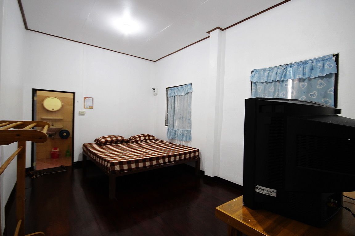 A small, compact room with a single bed, a television on a wooden stand, and a door leading to another room.