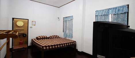 A small, compact room with a single bed, a television on a wooden stand, and a door leading to another room.