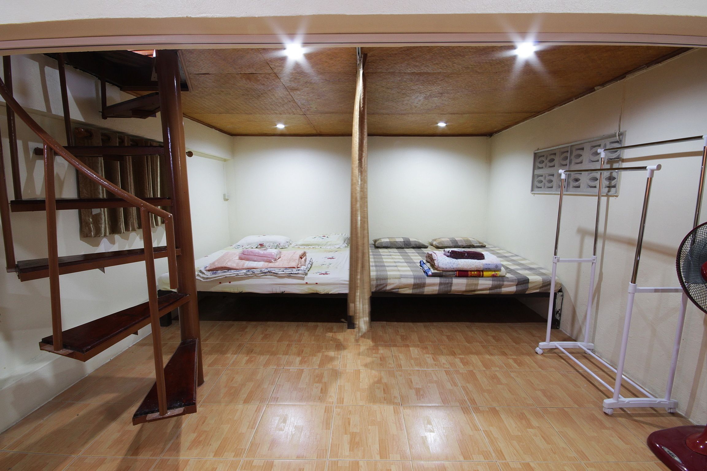 A room with two beds, a wooden staircase, a ceiling fan, and a radiator.