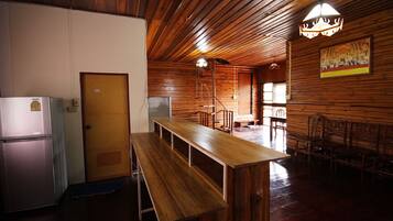 A wooden-paneled room with a long wooden table and benches, a refrigerator, and a door.