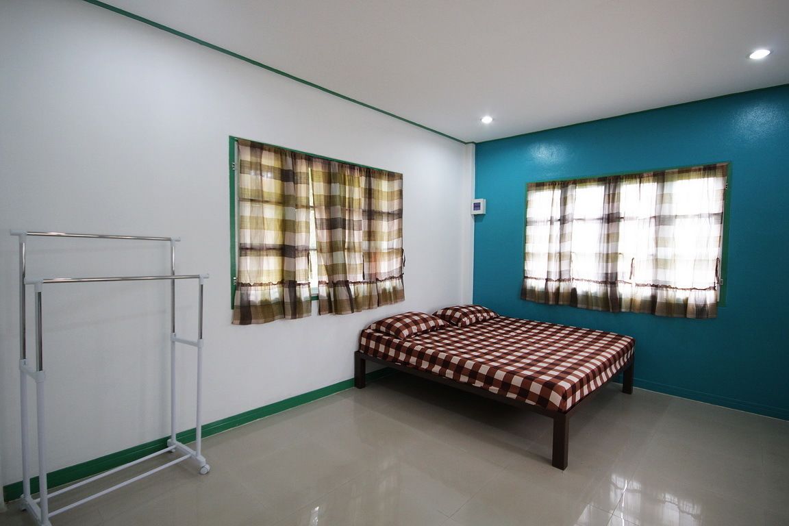 A room with a bed, a metal rack, and two windows with curtains.