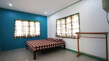 A room with a bed, two windows with curtains, a radiator, and a green trim along the wall.