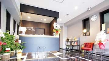 A hotel reception area with a reception desk, a clock, and a red chair.