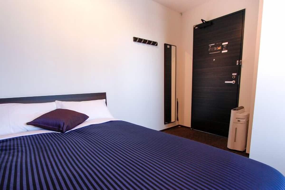 Una camera d'albergo con un letto, una porta scura e un piccolo oggetto bianco sul pavimento.