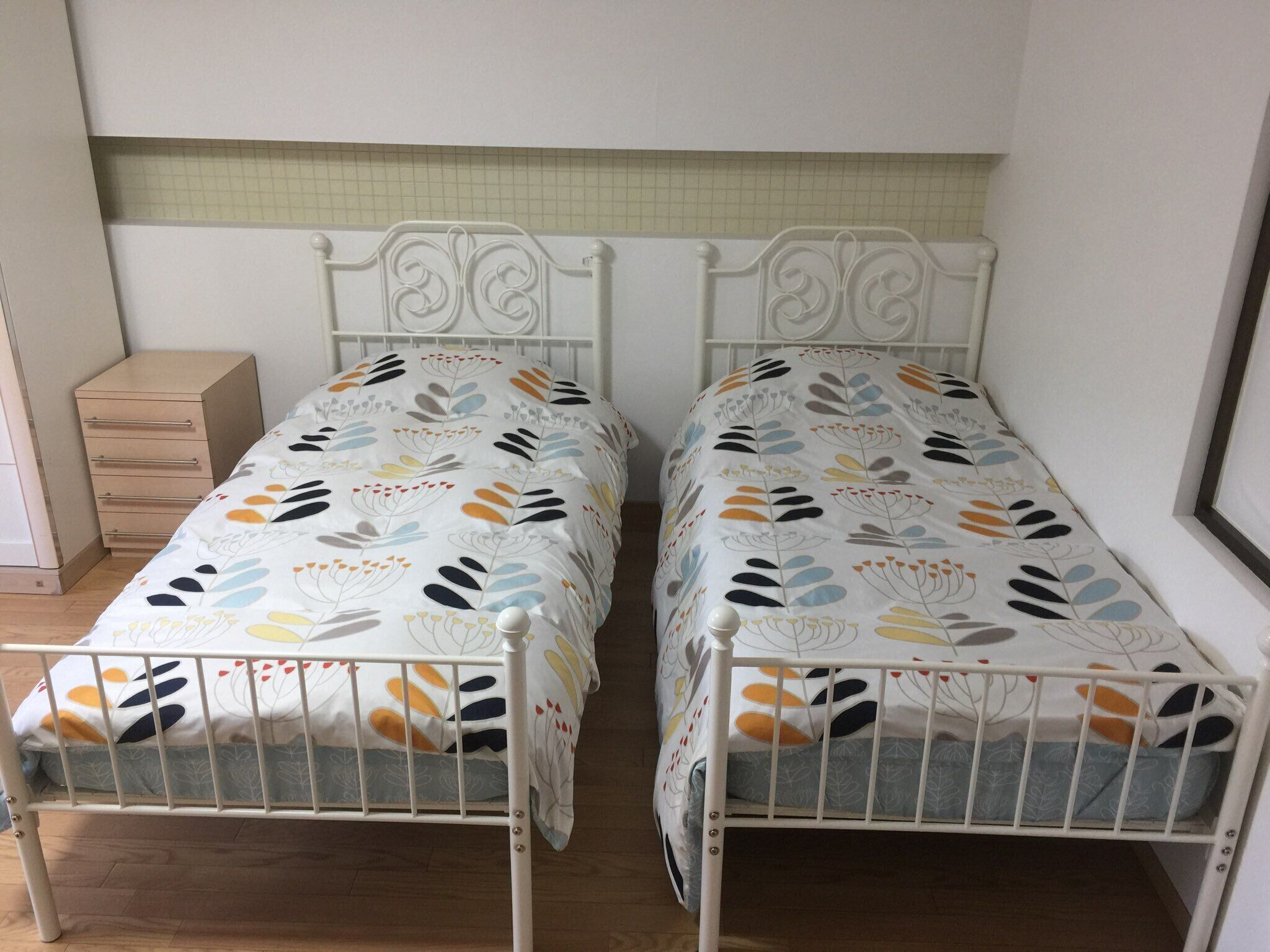 Two twin beds with a floral pattern, a wooden dresser, and a tiled backsplash.