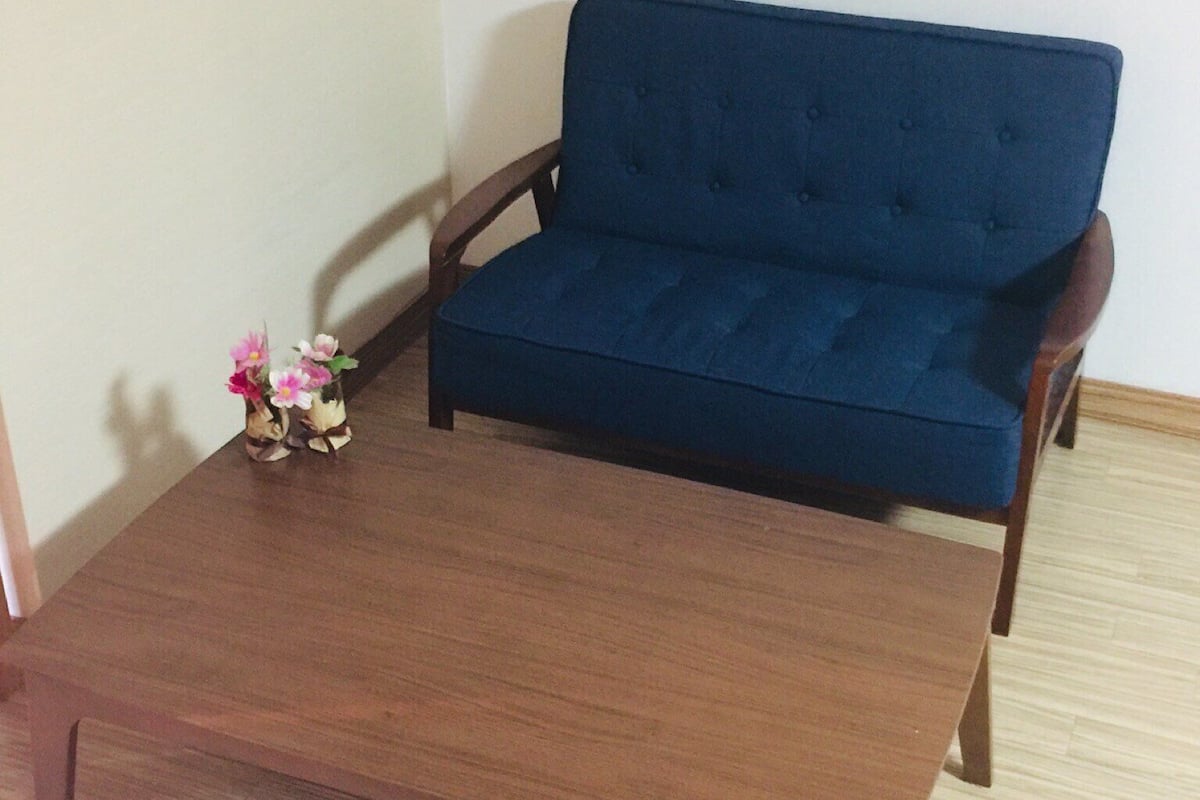 A dark blue sofa with wooden armrests and a wooden coffee table in a room with light-colored wooden flooring.
