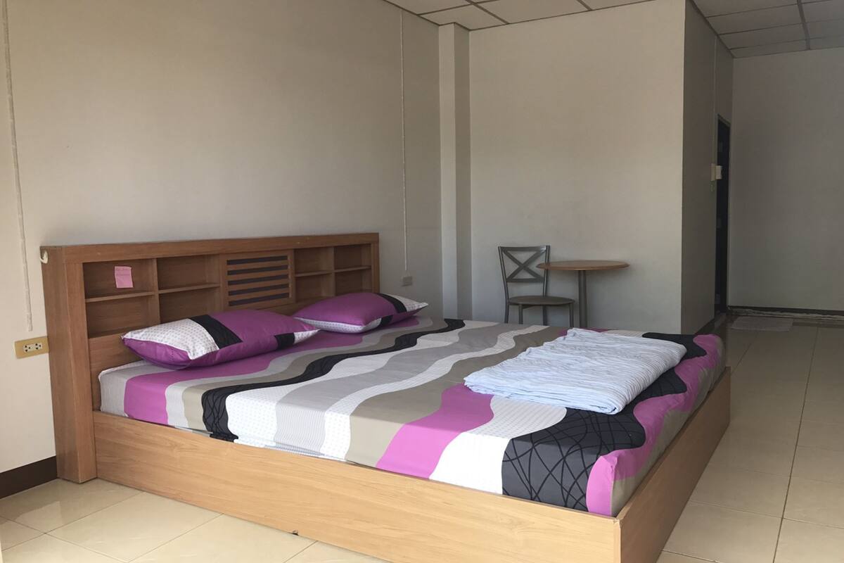 A neatly made bed with a wooden headboard and multiple pillows, a small table beside the bed, and a chair in the corner.