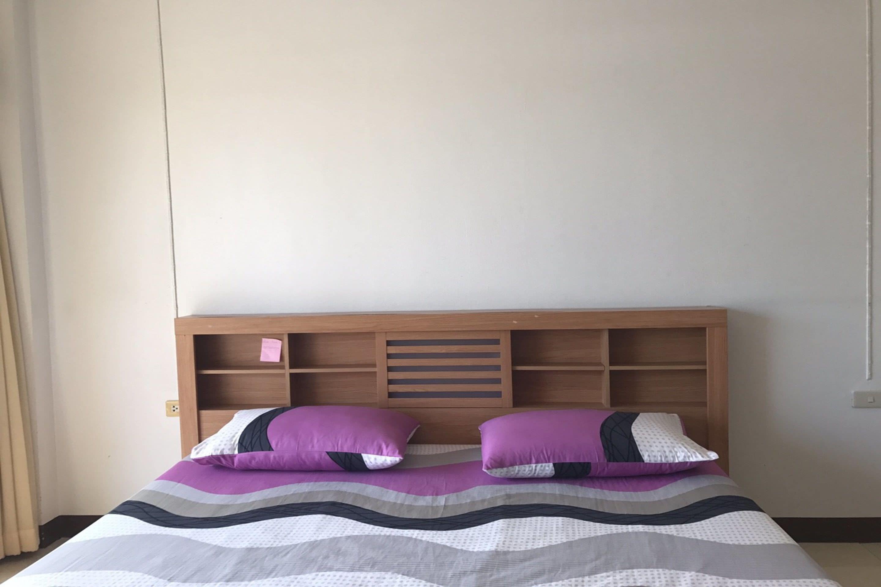 A bed with a wooden headboard, two purple pillows, and a striped bedspread.