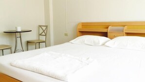 A neatly made bed with white linens, a small round table with a cup, and a chair to the left. - Eve Place Pattaya (Pattaya)