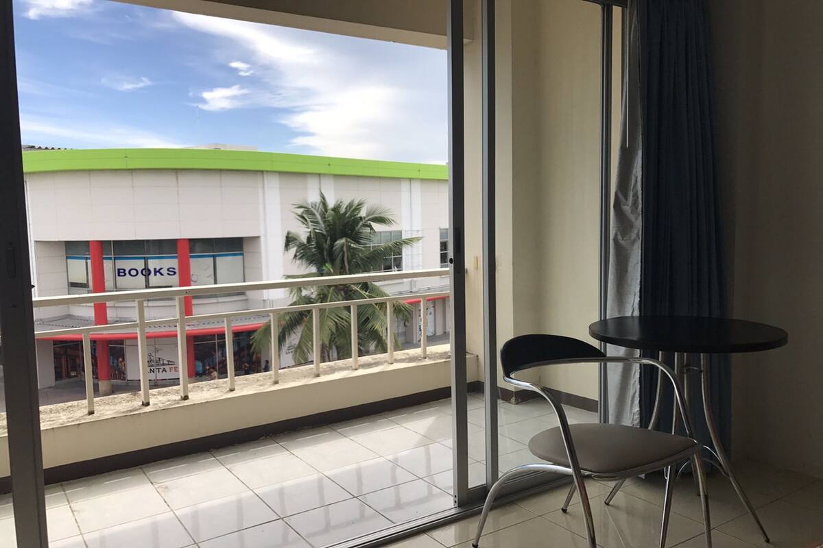 A balcony with a view of a building labeled 'BOOKS' and a palm tree. There are two chairs and a small table on the balcony.