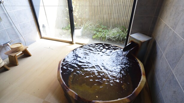 Een houten bad gevuld met water, een houten kruk en een raam met uitzicht op beplanting.