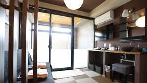 Een moderne hotelkamer met een bank, een kitchenette, een schuifdeur naar een balkon en een geruite vloer.