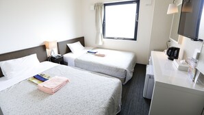 Een hotelkamer met twee bedden, een bureau, een spiegel, een raam met gordijnen en een airconditioner.