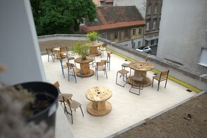An outdoor terrace with round wooden tables and chairs, surrounded by a low wall. - Lobagola B&B (Zagreb)