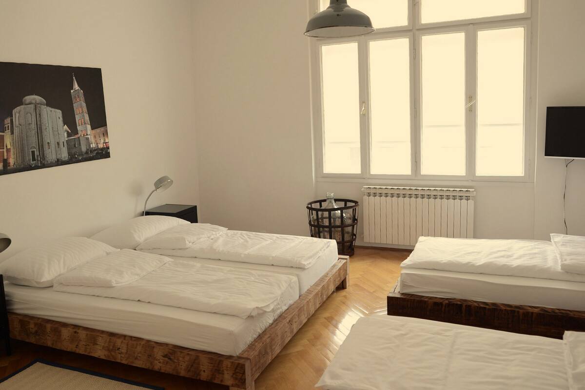 A room with two beds, a radiator, a window, and a painting on the wall.
